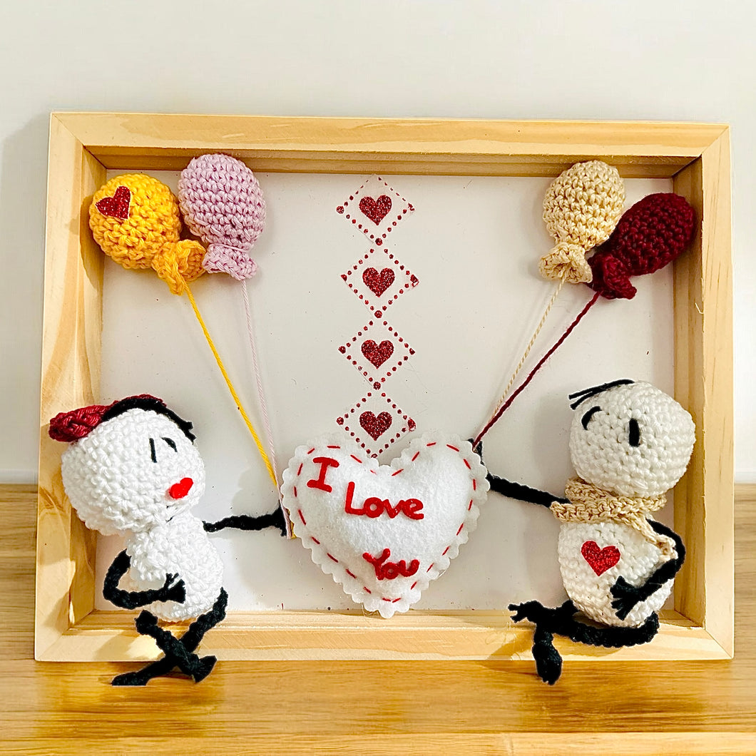 White crochet couple holding heart balloons with I Love You message in wooden frame
