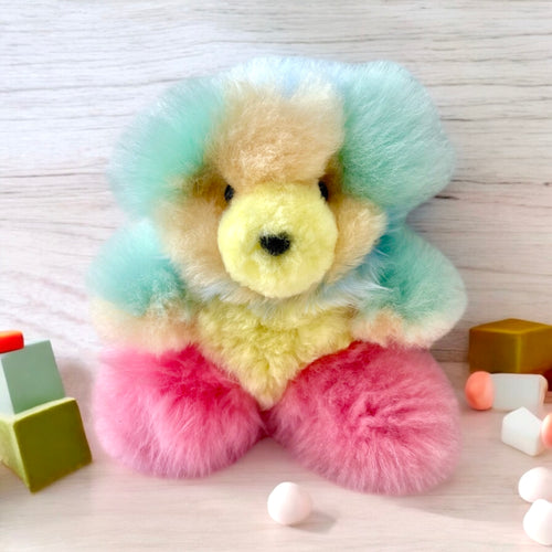 Single colorful Alpaca plush bear sitting on a light wooden surface with pastel blocks around it.